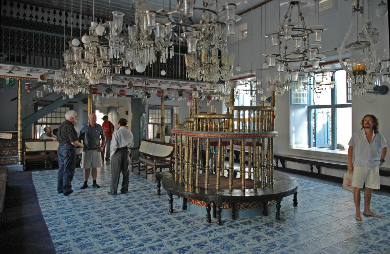 Interior of the Paradesi Synagogue in Kochi with blue patterned floor tiles, brass railings, and many glass chandeliers